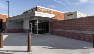 A modern detention center with a welcoming entrance features large glass doors, a brick facade, and blue skies overhead.