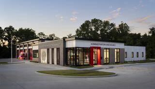 A modern fire station featuring a sleek design with a mix of brick and white exterior, complete with distinct red accents and surrounding greenery.