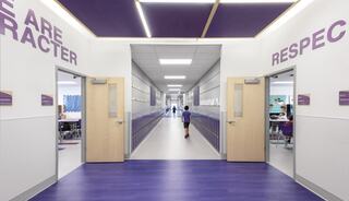 A brightly lit school corridor with purple accents and motivational words. A child walks toward classrooms on either side.