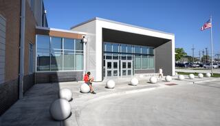 A modern building entrance features large spherical sculptures, with a child sitting nearby. A flag flies in a clear blue sky.