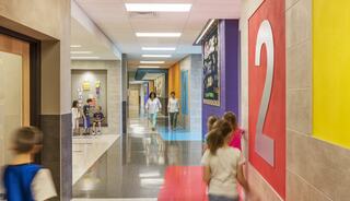 A vibrant school hallway features colorful walls, students walking, and teachers interacting, creating a lively educational atmosphere.