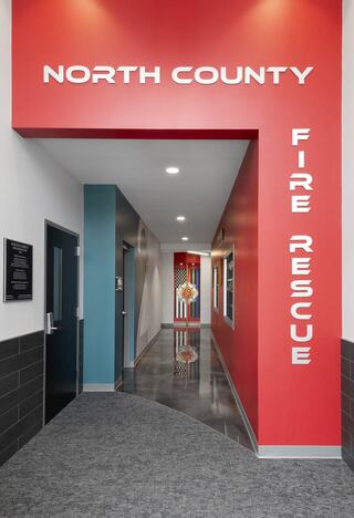 A modern hallway features red walls with "North County Fire Rescue" signage, illuminated by bright lighting and decorative elements.