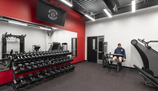 A modern gym featuring weights, exercise machines, and a person working out in a well-lit space with red and white walls.