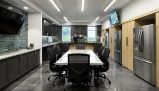 A modern kitchen features sleek cabinets, stainless steel appliances, and a large dining table surrounded by chairs, illuminated by bright lights.