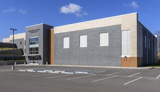 A modern, two-toned school building with large windows, surrounded by a parking lot and blue skies.