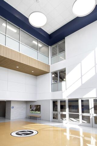 A spacious and modern athletic center features large windows, abundant natural light, and a sleek design, highlighting a central area with a logo on the floor.