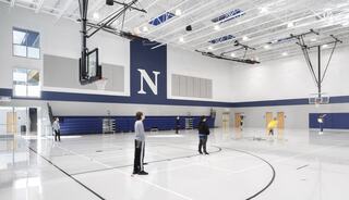 A spacious gym with a large "N" on the wall, featuring basketball hoops and people engaged in various activities. Bright and modern design.