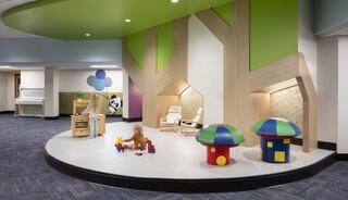 A colorful children's play area features play structures resembling trees, bright toys, and cozy seating for kids to explore and enjoy.