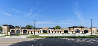 A modern, tan-colored building with large windows, surrounded by greenery and a clear blue sky, features an elegant design and spacious layout.