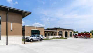 A modern public safety facility features emergency vehicles and a spacious parking area under a clear blue sky.