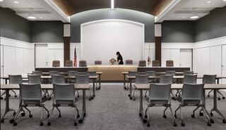 A modern courtroom with a central bench, several chairs arranged in rows, and a subdued color scheme enhancing a formal atmosphere.