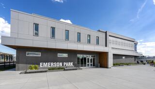 A modern building with a sleek design features large windows and a sign reading "EMERSON PARK," set against a bright blue sky.