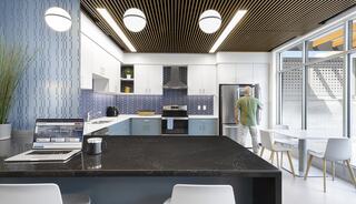 A modern kitchen features sleek cabinets, a dark countertop, and a person standing near a fridge, with bright lighting and a laptop on the island.