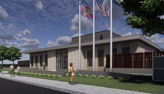 A modern building with large windows, surrounded by greenery, displaying multiple flags and a clear sky, with people walking nearby.