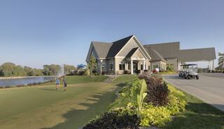 A well-maintained golf course features a clubhouse near a serene lake, with golfers enjoying the lush surroundings and clear skies.