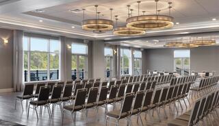 A spacious room featuring rows of neatly arranged chairs, large windows with scenic views, and elegant lighting fixtures.