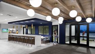 A contemporary lounge area features a sleek bar with seating, modern lighting, and large windows, creating a welcoming atmosphere.