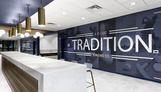 A modern reception area featuring a sleek counter and a wall displaying "TRADITION REMAINED 2021" with various sports imagery.