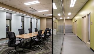 A modern office space features a glass-enclosed conference room with a large table and chairs, alongside a corridor with doors.