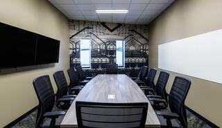 A modern conference room featuring a large table, black ergonomic chairs, two screens, large windows, and a stylish patterned wall.