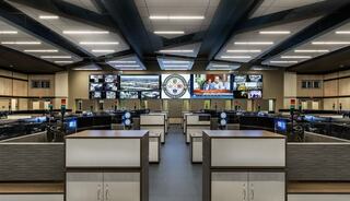 A modern command center features rows of desks, multiple screens displaying data, and a sleek design, emphasizing a high-tech operational atmosphere.