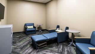 A small, modern lounge with blue chairs, a recliner, and a TV mounted on the wall, featuring a stylish zigzag floor.