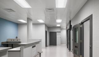 A modern, sterile corridor with bright lighting, featuring a reception area, closed doors, and light blue accent walls.