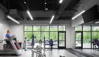 A modern gym features a treadmill, weight machines, and large windows showcasing greenery outside, creating a bright, inviting workout space.