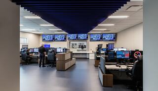 A modern control room featuring multiple screens, workstations, and personnel engaged in monitoring activities. Bright and spacious layout.