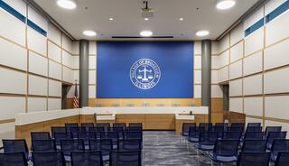A modern courtroom featuring rows of blue chairs, a large emblem on the back wall, and a clean, minimalist design.