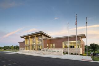 A modern municipal center features a sleek design, large windows, and flags in front, set against a clear sky and green landscape.