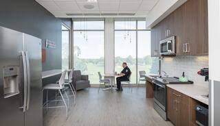 A modern kitchen space features sleek appliances, comfortable seating, and large windows offering a view of greenery outside.