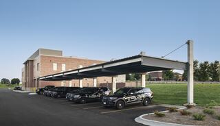 A parking area with several police vehicles lined up beside a modern brick building under a covered structure, surrounded by green space.