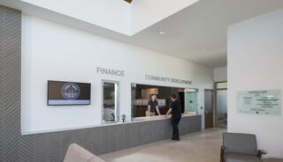 A modern reception area with a counter labeled "Finance" and "Community Development," features two people interacting in a well-lit space.