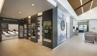 A modern office foyer features a boardroom entrance, exhibit displays, and a comfortable waiting area with ample natural light.