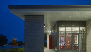 A modern building entrance with glass doors and a sleek design, illuminated at night, showcasing a welcoming ambiance.
