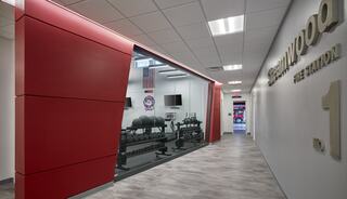 A modern fire station corridor features sleek design elements, with a fitness area visible through glass, showcasing gym equipment.