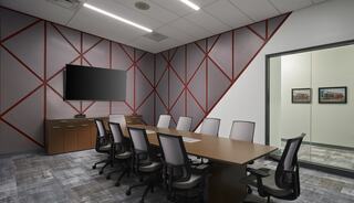 A modern conference room featuring a long table, ergonomic chairs, a wall-mounted TV, and stylish geometric wall design.