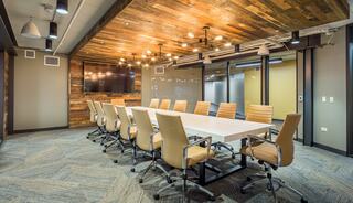 A modern conference room features a long, white table, ergonomic chairs, rustic wooden ceiling, and warm lighting for a cozy atmosphere.