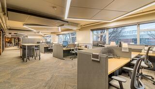 A modern, spacious office layout featuring cubicles, ergonomic chairs, and large windows providing natural light.