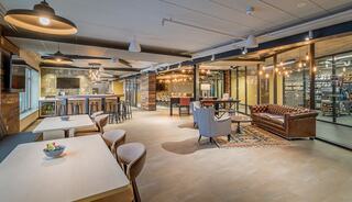 A modern, stylish lounge with a bar area, cozy seating, wood accents, and decorative lighting, creating an inviting social space.