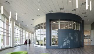 A modern, spacious interior with large windows, sleek design, and a mural featuring basketball players. Green seating adds a pop of color.