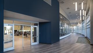A modern, spacious hallway features large windows, with sleek lighting and an entrance leading to a gym area in the background.