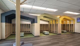A bright, modern space features cubby lockers with colorful arches, green carpet, and seating, creating an inviting atmosphere.