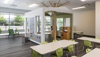 A bright, modern classroom features a playhouse structure, colorful seating, and spacious tables, promoting a fun learning environment.