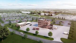 Aerial view of a fire and emergency services facility with a large parking lot, surrounded by green spaces and a nearby lake.
