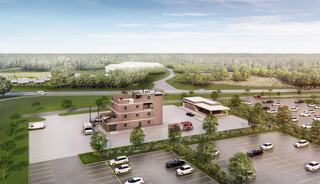 Aerial view of a modern facility with a parking lot, green surroundings, and multiple buildings, including a larger structure and a fire station.