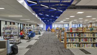 A modern library featuring stylish shelves of books, comfortable seating, and a striking blue ceiling design, bustling with study activity.