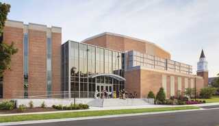 A modern brick building features large glass windows, an inviting entrance, and manicured landscaping, surrounded by a peaceful setting.