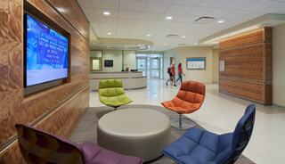 A modern lobby features colorful chairs, a circular table, and digital displays, creating a welcoming atmosphere with bright, open spaces.